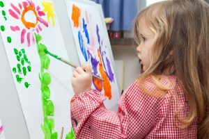Cute little blond girl holding brush and painting on paper