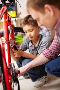 Portrait of little boy and his father repairing bicycle in garage